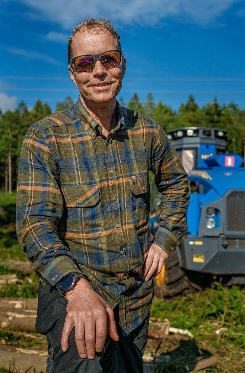 Föraren i rutig skjorta framför den blå skördaren
