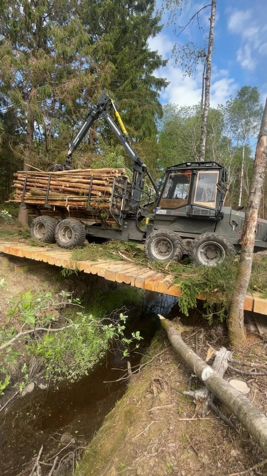 Lastad skotare kör över en bro av virke över en bäck